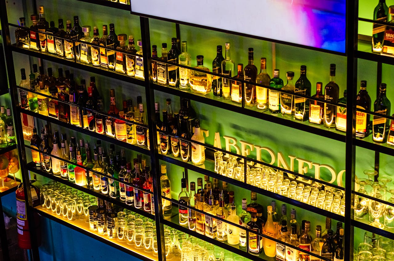 Illuminated bar shelves showcasing various liquor bottles and glasses in a vibrant setting.